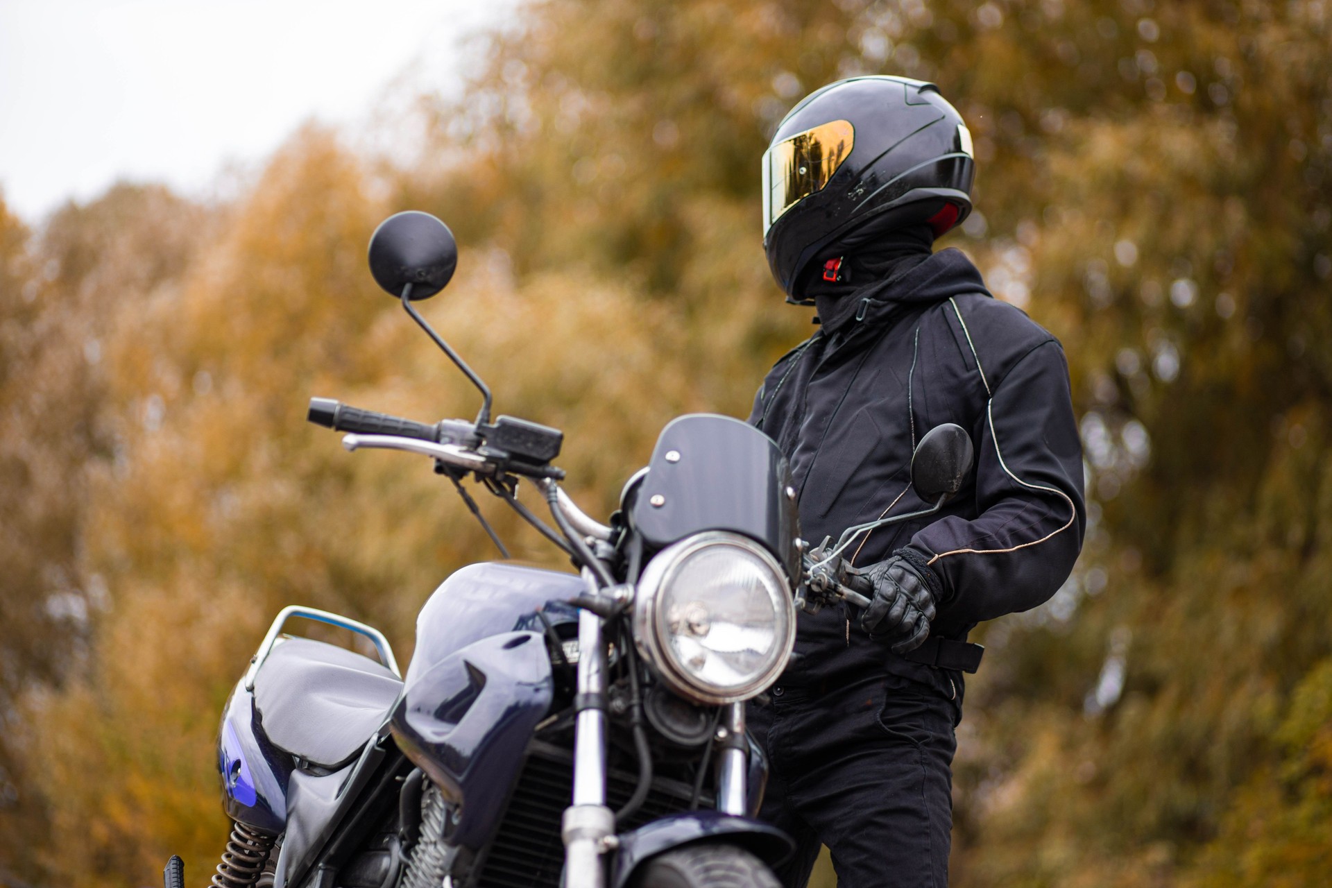 motorcyclist in a motorcycle jacket and tinted helmet with a classic motorcycle in nature. Stylish biker